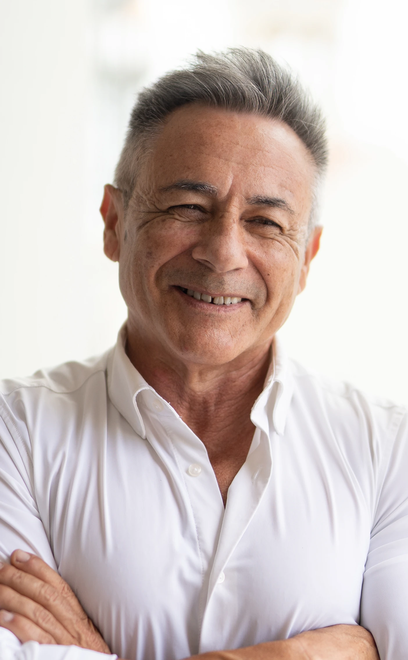 Imagen de un hombre mayor sonriendo a cámara con los brazos cruzados.