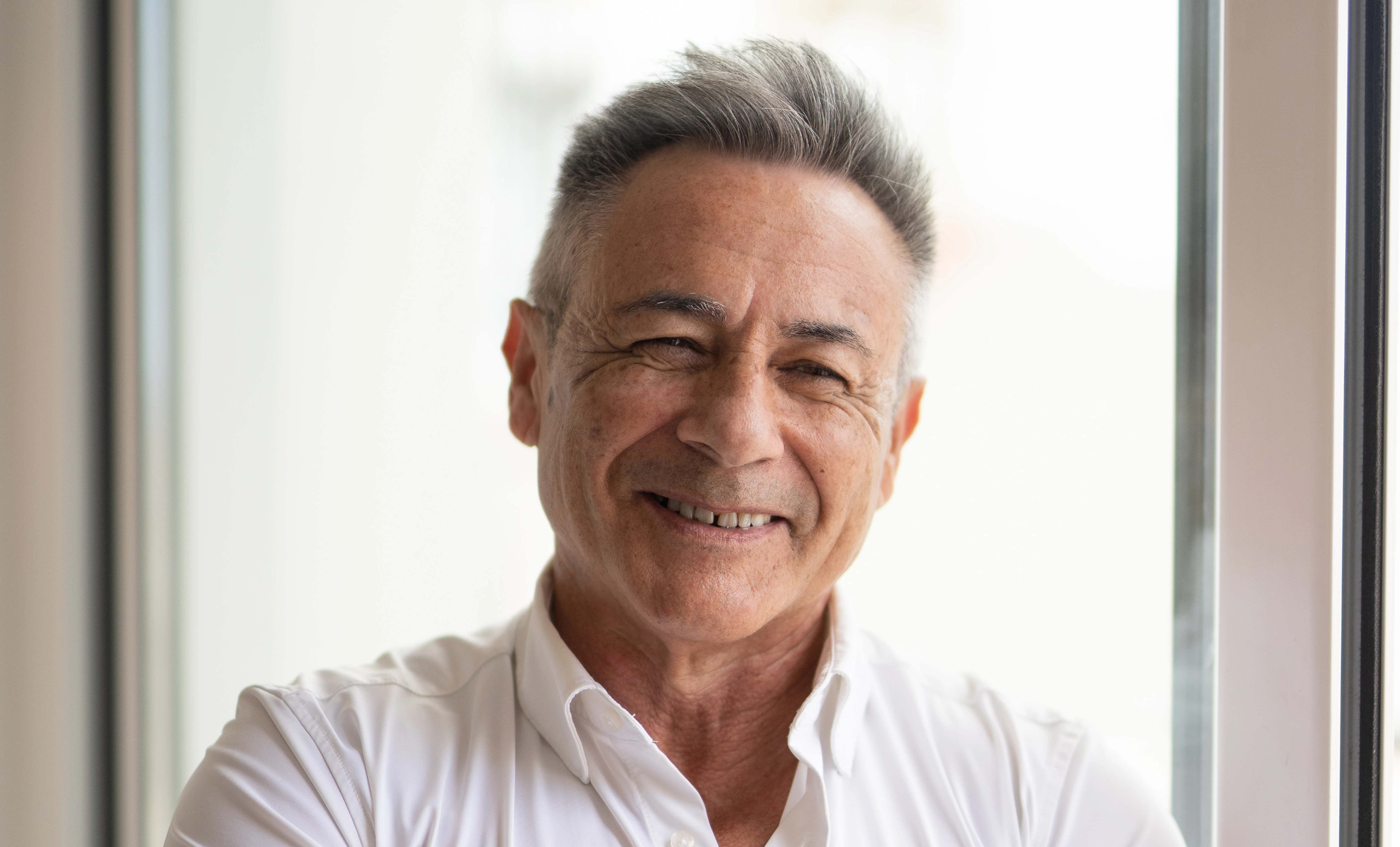 Imagen de un hombre mayor sonriendo a cámara con los brazos cruzados.
