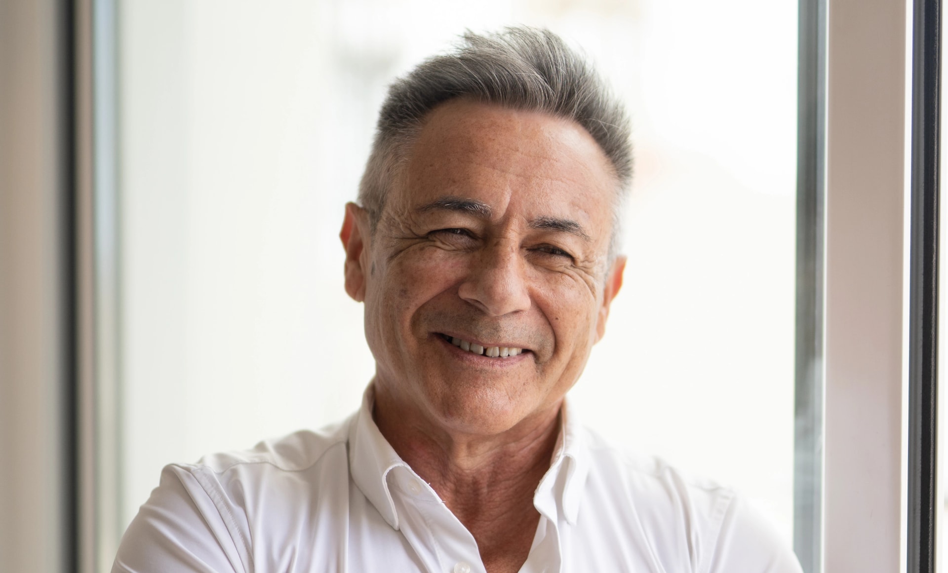 Imagen de un hombre mayor sonriendo a cámara con los brazos cruzados.